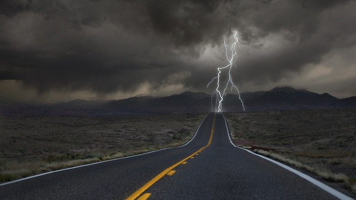 Road leading to mountains during a lightning storm