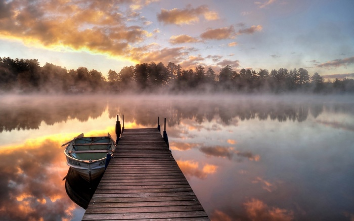 Wooden dock and boat on a misty lake at sunrise