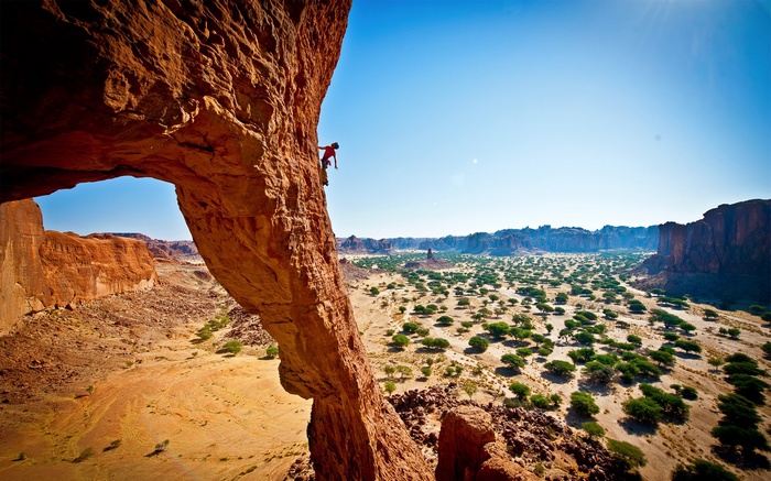 Rock climber on a natural arch in a desert landscape