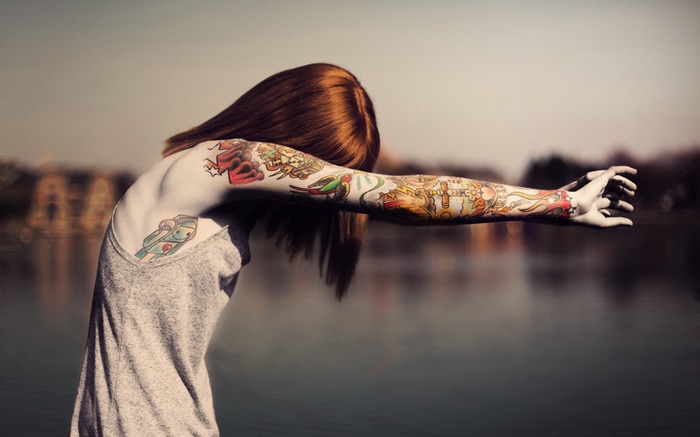 Woman with full sleeve tattoos by the water