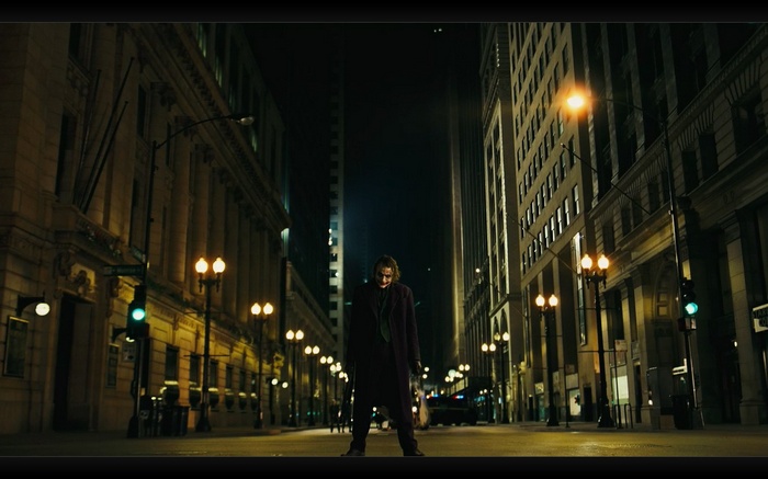 The Joker stands in the middle of a city street at night