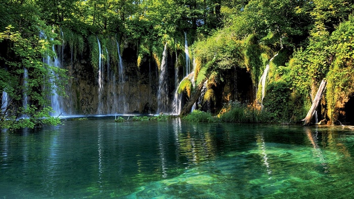 Waterfalls cascading into a clear turquoise lake surrounded by greenery