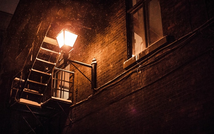 Snow falling on a brick building with a lit lantern