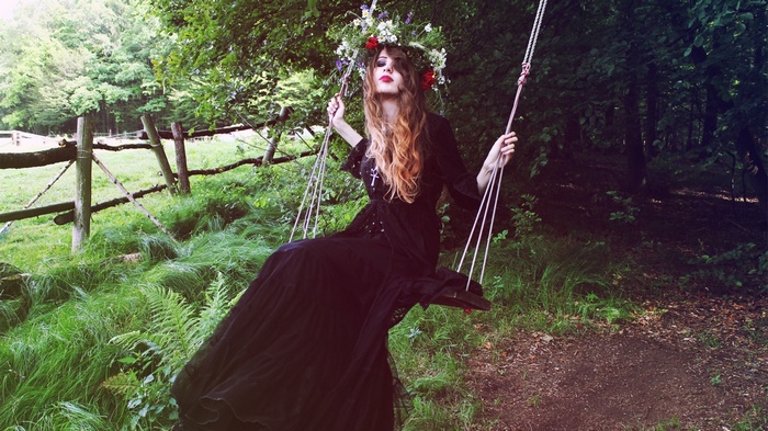 Woman with flower wreath on swing in forest