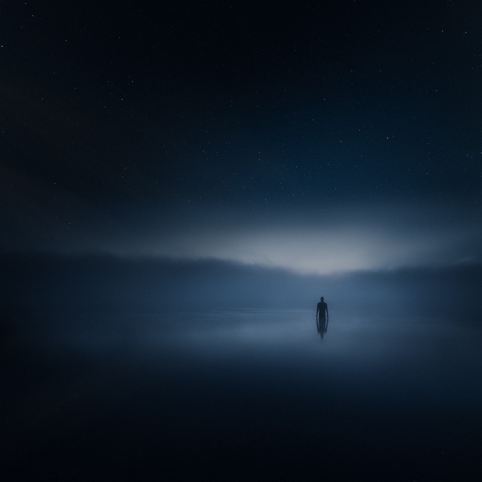 Man standing in water under starry night sky with mist