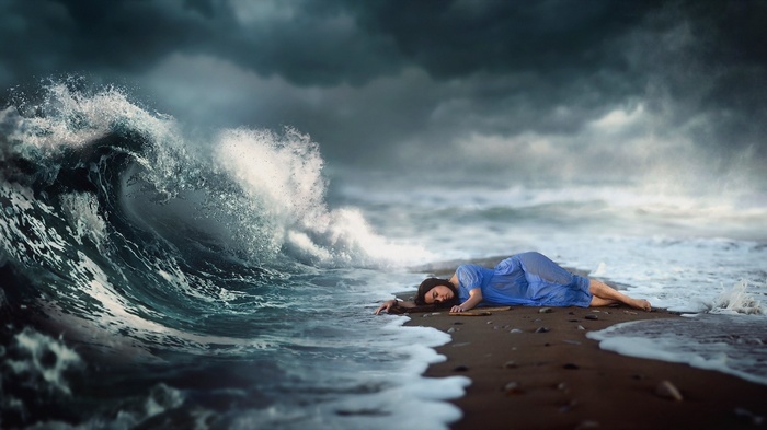 Woman in blue dress lying on beach with stormy waves