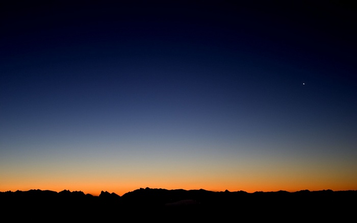 Silhouette of mountains against a sunset sky with a bright star