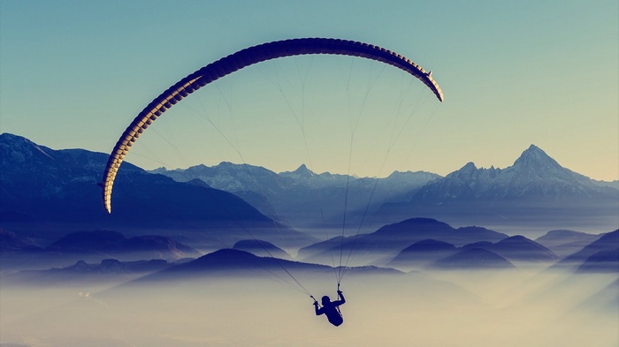 Paraglider soaring over misty mountains at sunset