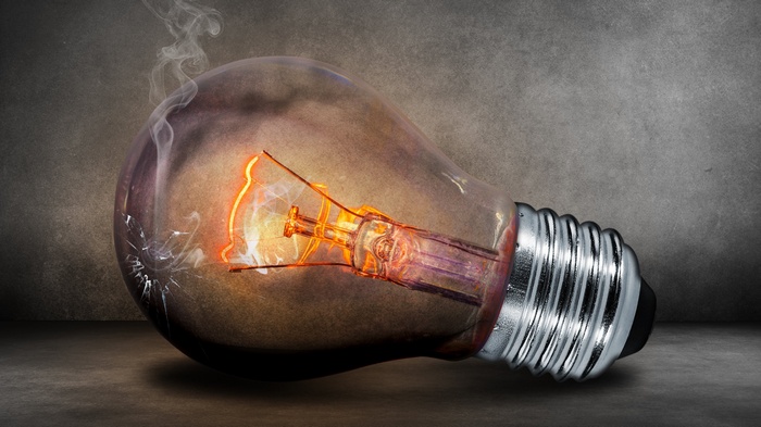 Broken light bulb with glowing filament and smoke