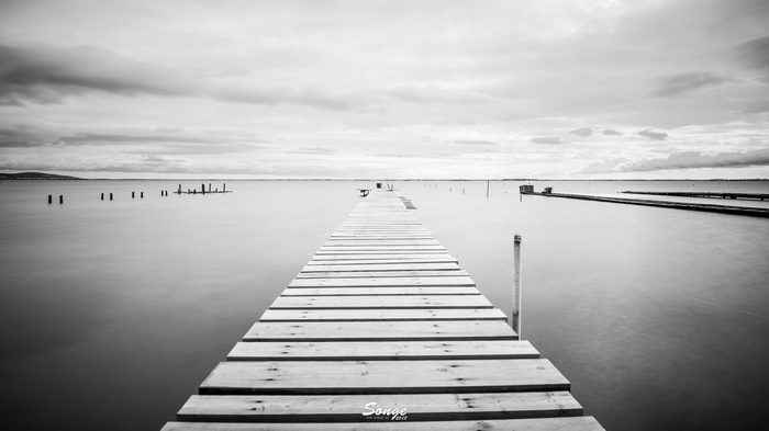 Wooden pier extending into calm water under cloudy sky