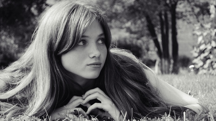 Monochrome portrait of a young woman with freckles lying in grass