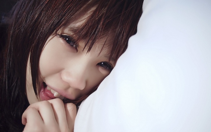 Asian woman peeking from behind a white pillow