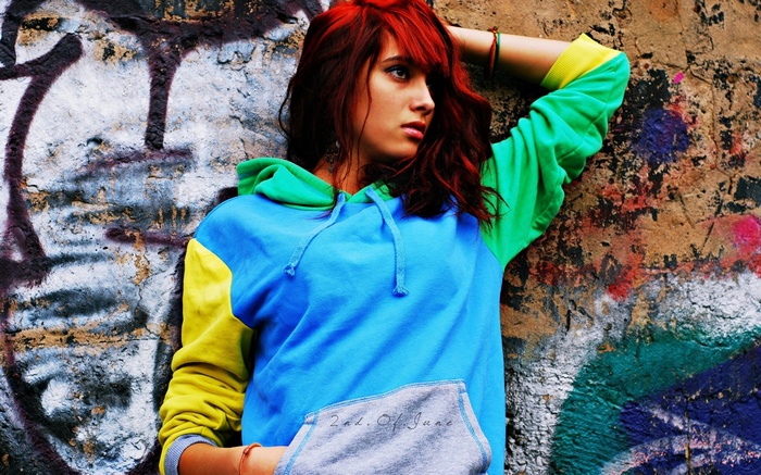 Woman with red hair leaning against graffiti wall