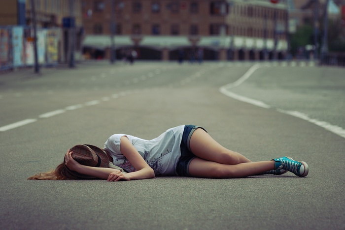 Woman in hat lying on a city street