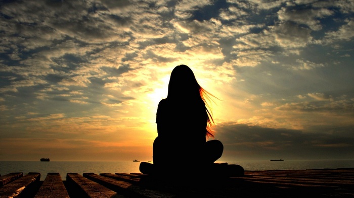 Woman sitting on wooden planks at sunset