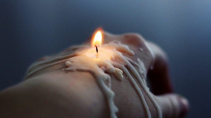 Candle wax dripping on a hand with a flame