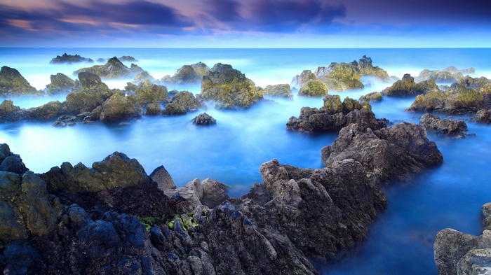 Rocky coastline with misty blue ocean and purple clouds