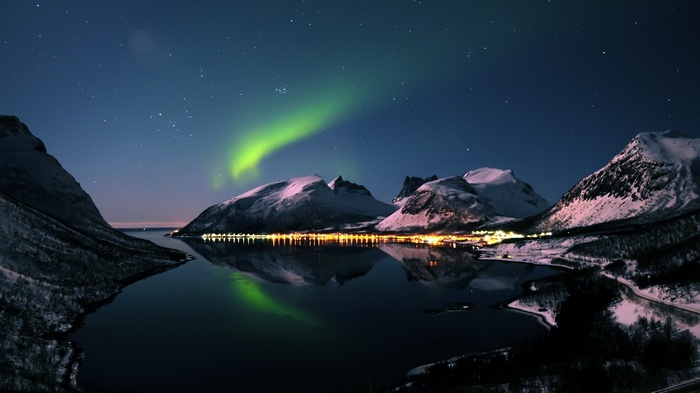 Aurora borealis over snow-capped mountains and a town