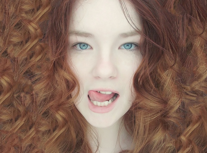 Woman with curly red hair and blue eyes sticking out her tongue