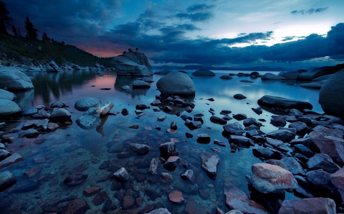 Rocky shore of a lake at dusk with dramatic clouds