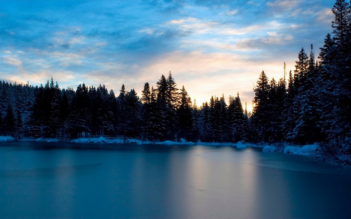 Winter forest landscape with frozen lake at sunset