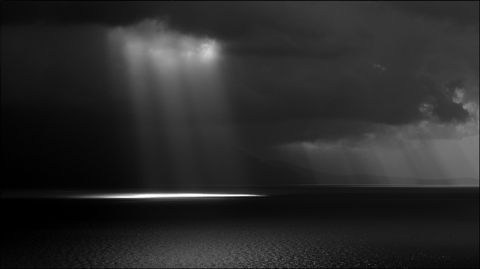 Monochrome sea with dramatic sunbeams through clouds