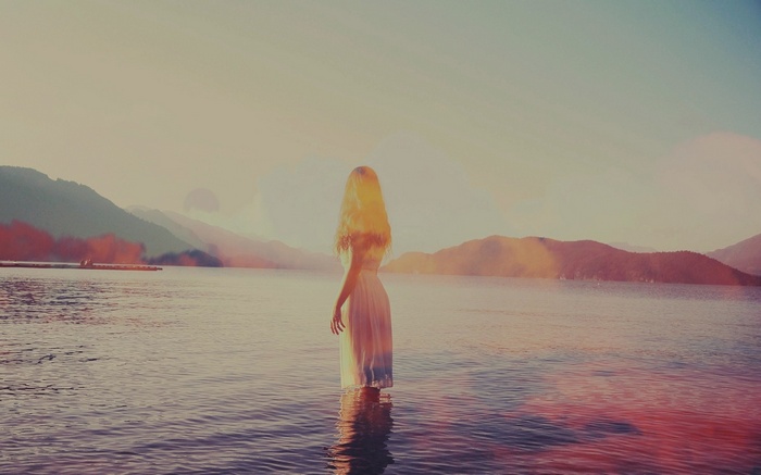 Woman in white dress standing in water at sunset