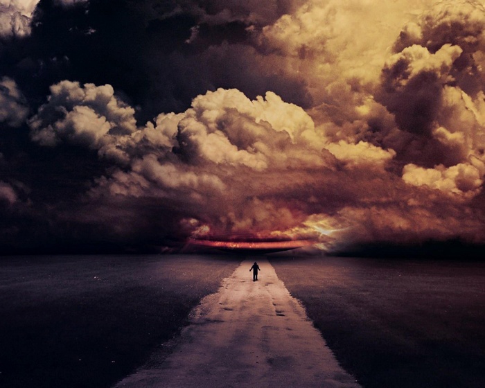 A person walks on a road under dramatic clouds