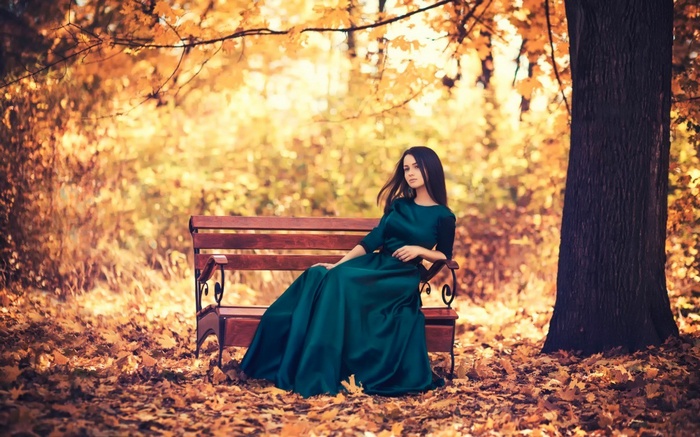 Woman in a green dress sitting on a bench in autumn