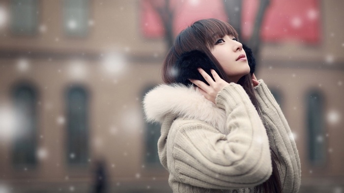 Asian woman wearing earmuffs and sweater in snow