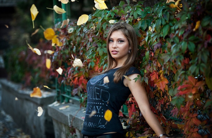 Woman leaning against a wall of colorful fall leaves