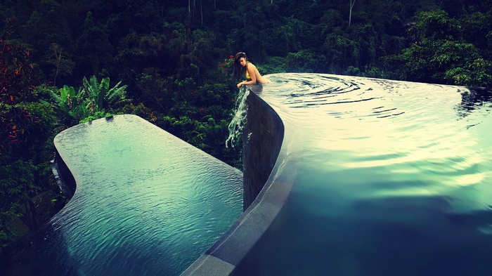 Woman in bikini at infinity pool overlooking jungle