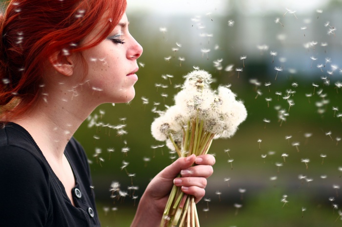Redhead woman blowing dandelions outdoors