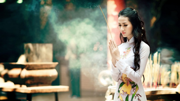 Woman in traditional Vietnamese dress praying with incense