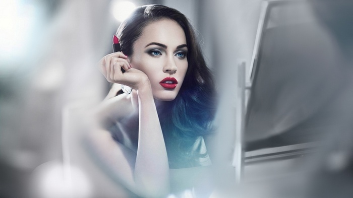 Megan Fox applying red lipstick in front of a mirror
