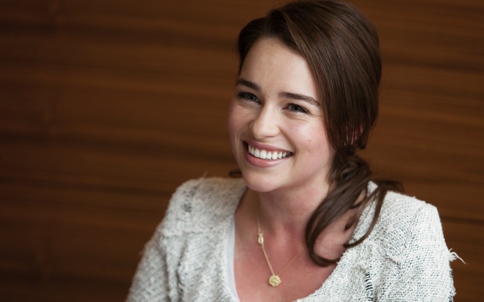 Emilia Clarke smiling wearing a necklace and sweater