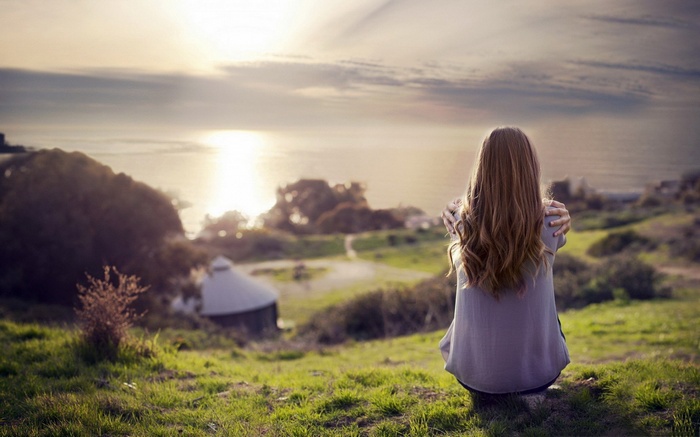 Woman with long hair sitting outdoors at sunset