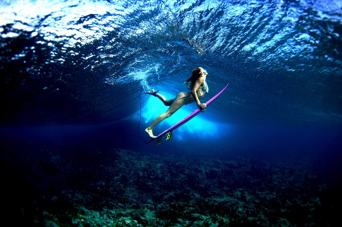 Woman surfing underwater on a purple surfboard