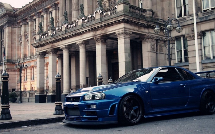Blue Nissan Skyline R34 GT-R parked in front of classical architecture