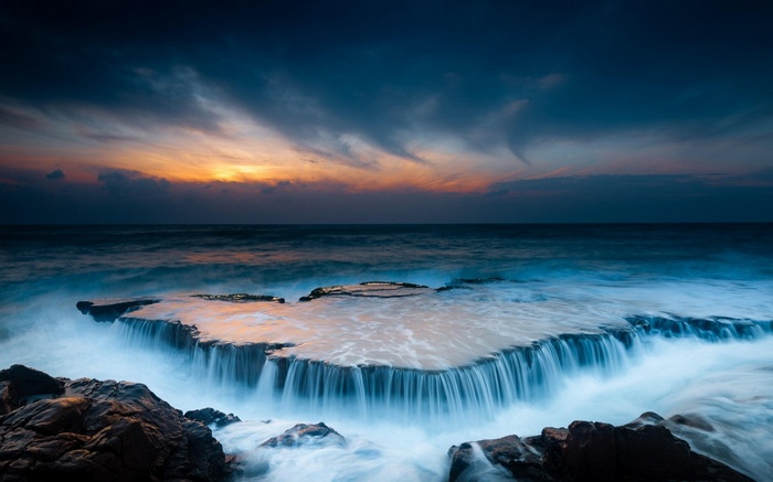 Sunset over ocean waves crashing on rocks
