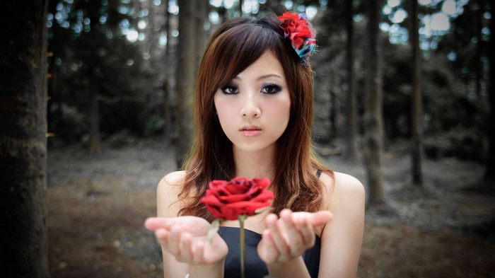 Asian woman holding a red rose in a forest