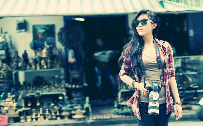 Asian woman with sunglasses and camera in front of a shop