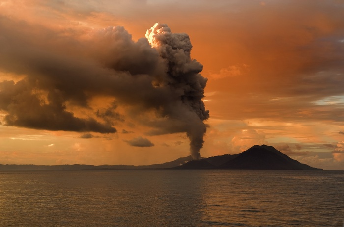Volcano eruption spewing smoke over the sea at sunset