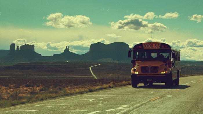 Yellow school bus driving on a road in Monument Valley