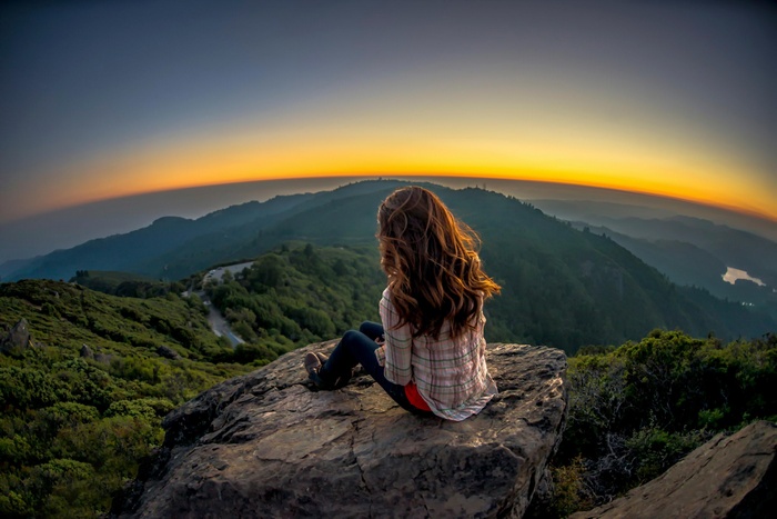 Woman sitting on a rock overlooking mountains at sunset