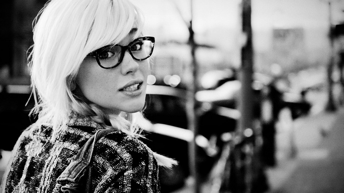 Woman with blonde hair and glasses looking over her shoulder