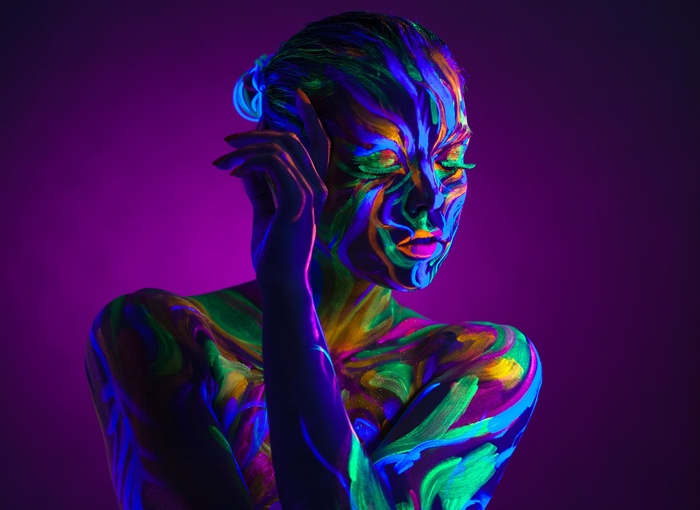 Woman with neon body paint on purple background