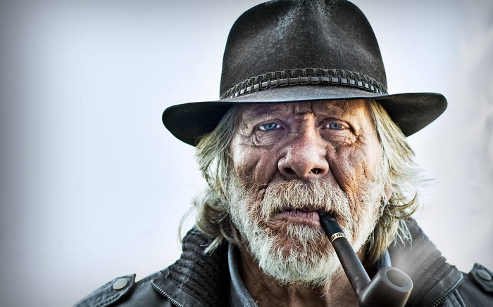 Old man with blue eyes smoking a pipe and wearing a hat