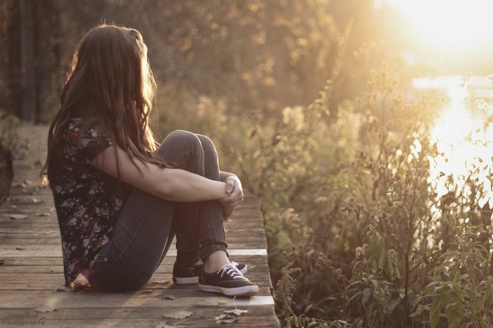Woman sitting on a wooden dock at sunset
