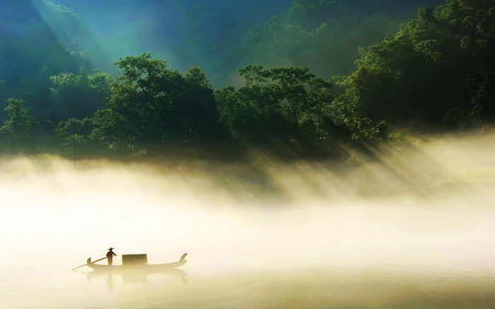 Boat on misty river with sunbeams through forest